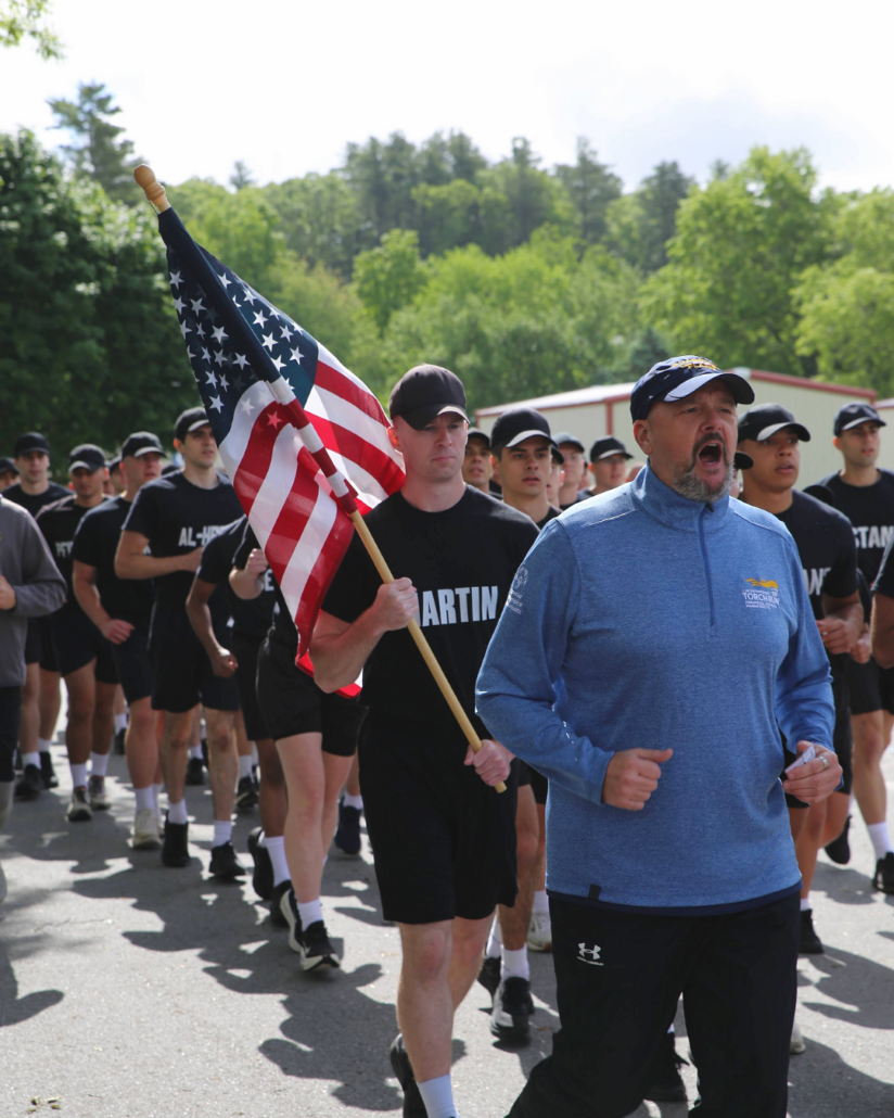 student officers in black shirts and shorts carry flag