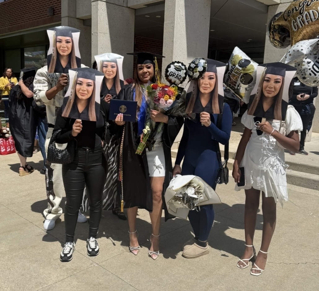 yulissa poses in her graduation cap and gown surrounded by friends holding up giant cutouts of her head