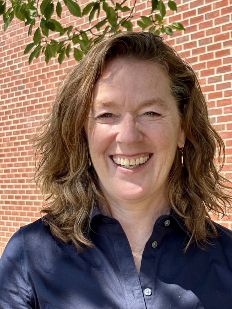 Laura smiles at the camera, posed for a headshot in front of a brick building 