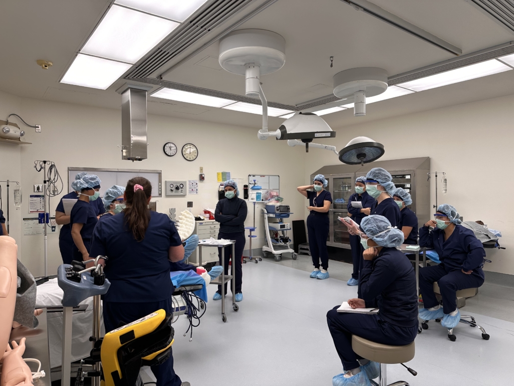 students wearing blue scrubs, masks and hair covers gather together in a surgical lab