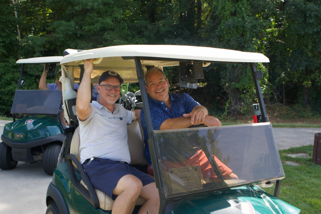 two men in a golf cart smile at camera
