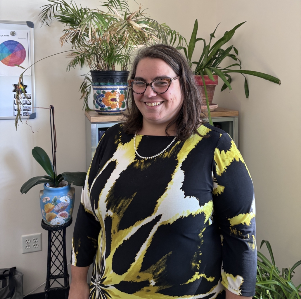 jennifer stands in front of a shelf of plants smiling at the camera
