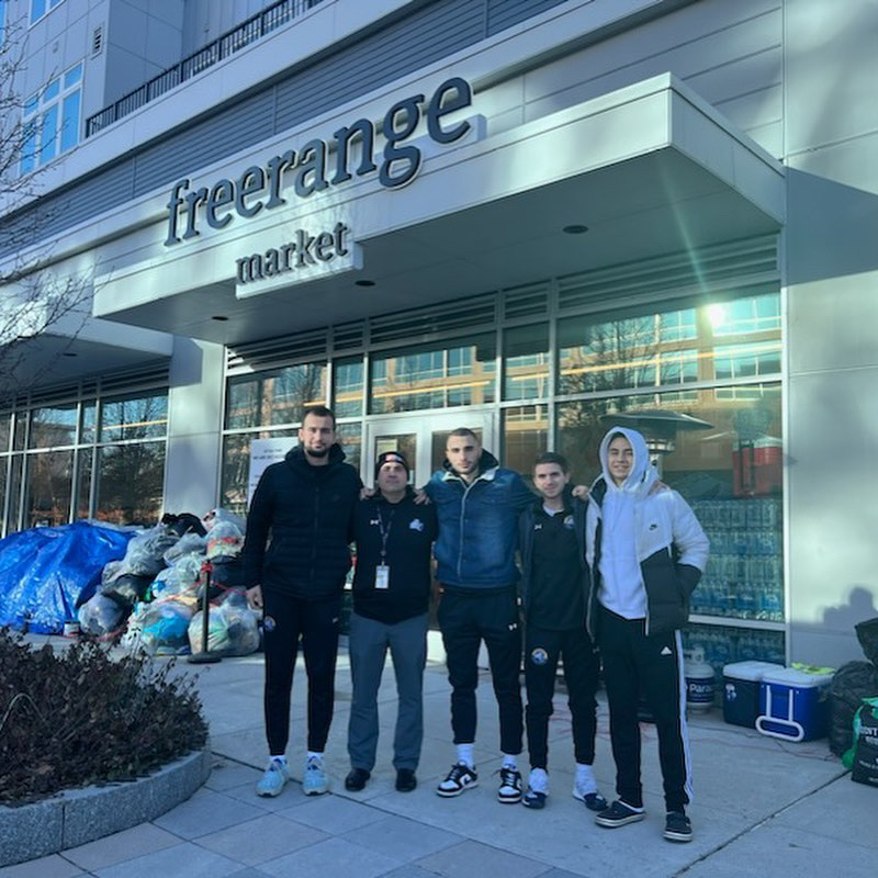 five men pose in front of market with bags of donated items