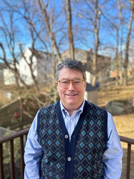james, wearing blue button down shirt and plaid vest, smiles at the camera