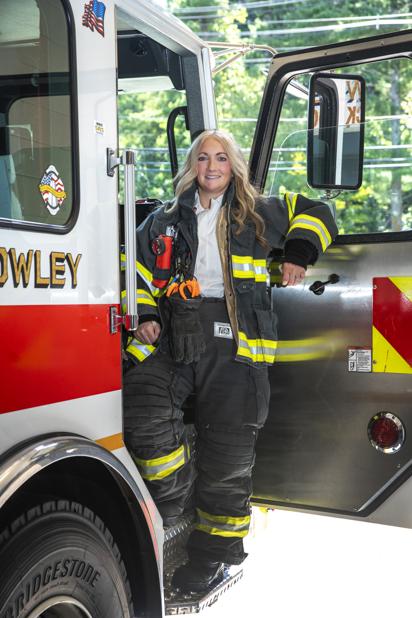 Merissa poses in fire fighter's gear in doorway of truck