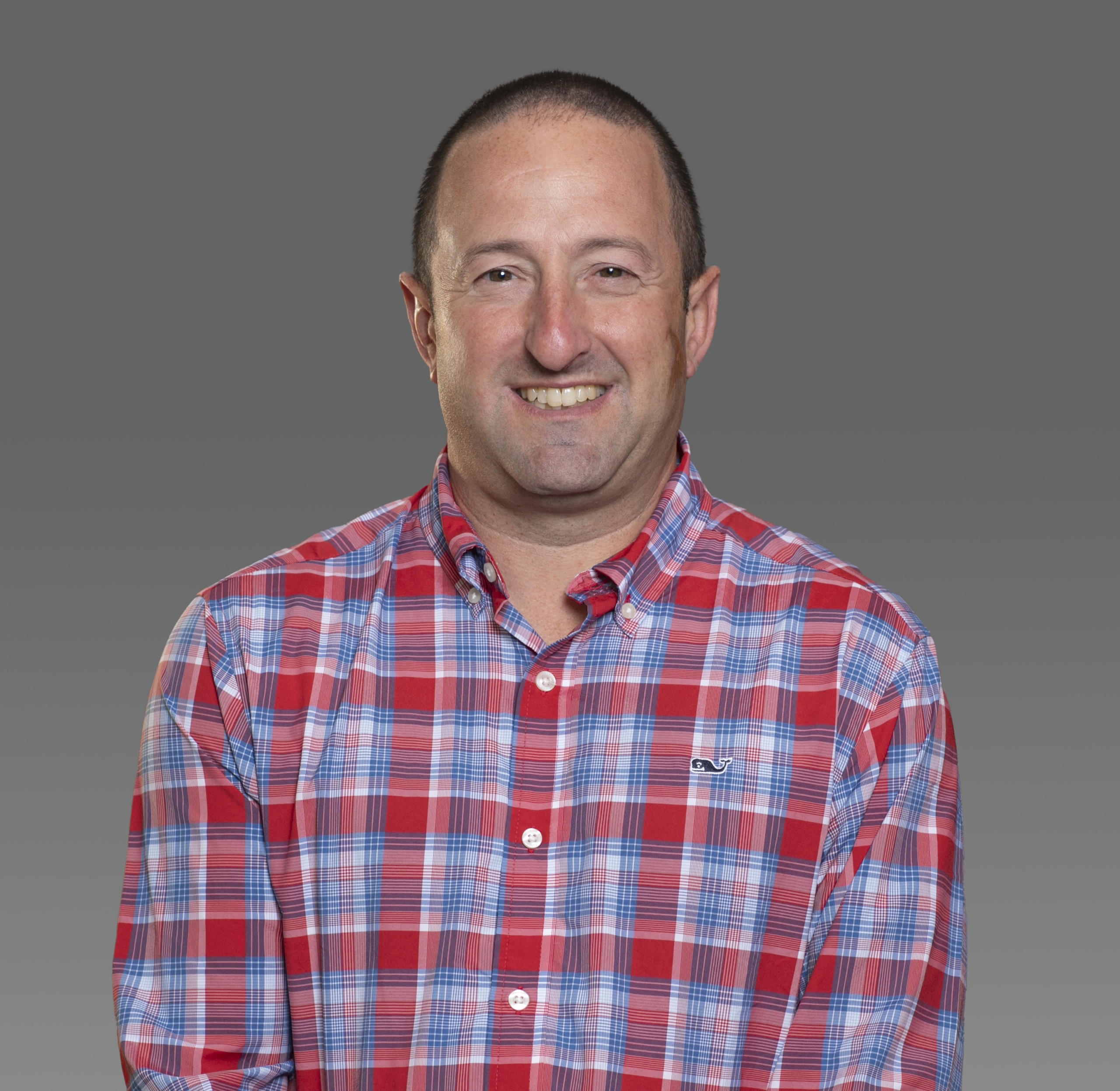 dan, wearing a blue and red checkered shirt, smiles at the camera in front of a grey backdrop