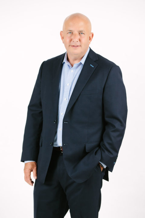 michael stads in dark suit and light blue shirt smiling at camera