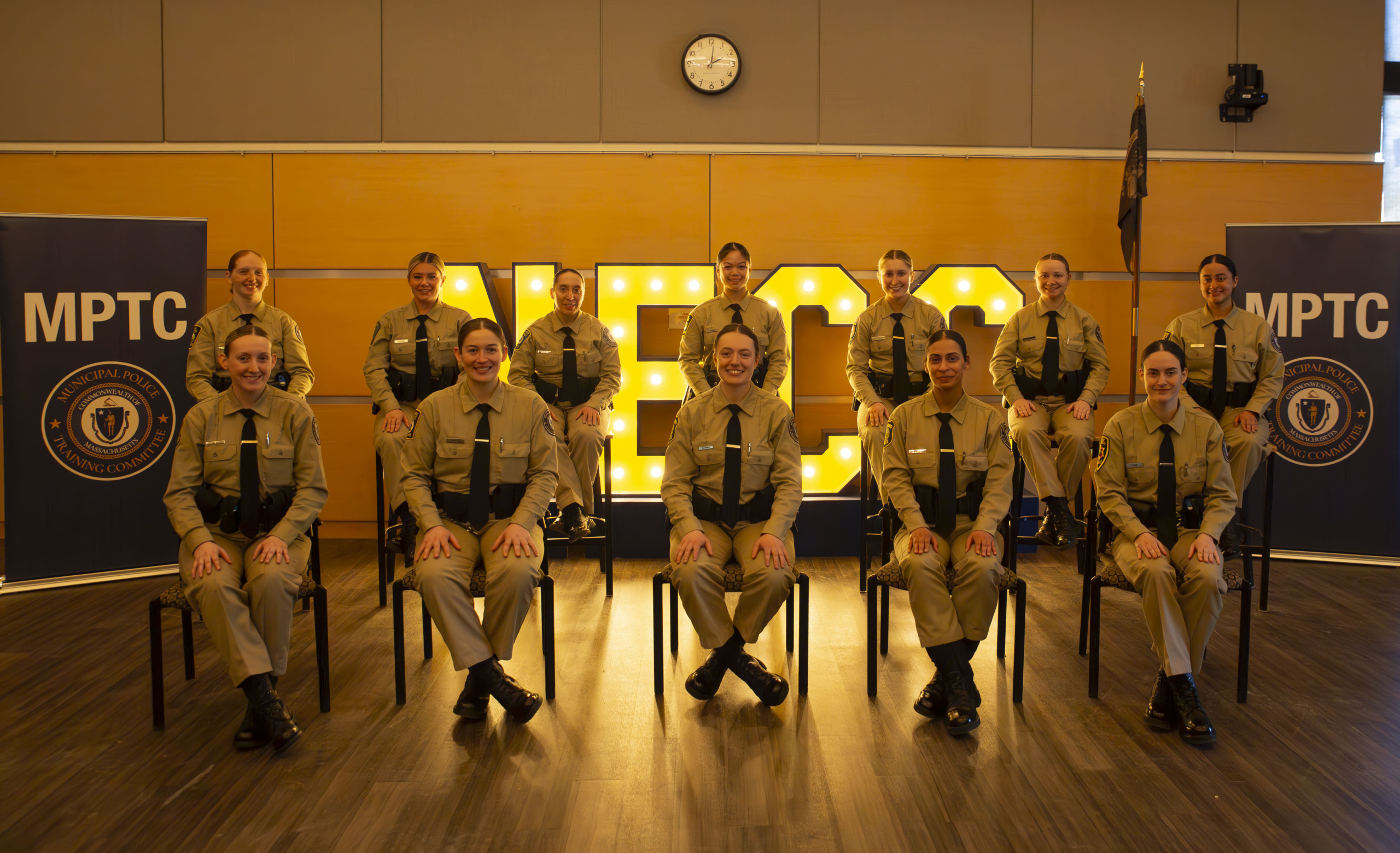 photo of the 12 female student officers in the NECC MPTC academy, sitting in front of a marquee of the NECC letters
