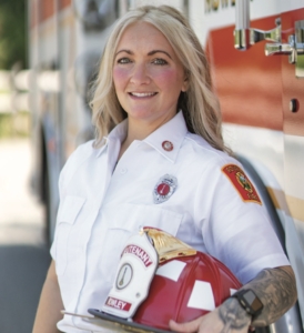 Merissa leaning against a fire truck, holding helmet