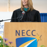 congresswoman trahan stands behind podium with NECC logo with Commencement regalia