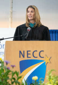 congresswoman trahan stands behind podium with NECC logo with Commencement regalia
