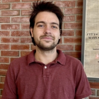 nick smiles at the camera in front of brick background