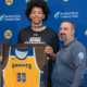 delgado stands next to darren stratton, holding framed yellow jersey with his name and number 30 on it