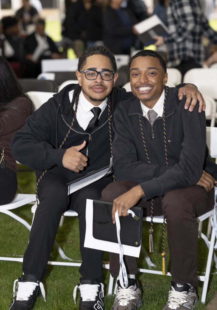 two young men, dressed in shirts and ties with a quarter zip smile at the camera