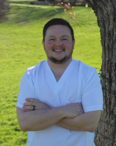 photo of NECC nursing student Kaleb Bradish in white scrubs outdoors