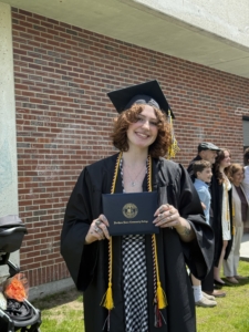 mckenzie stands wearing cap and gown at commencement, holds her diploma