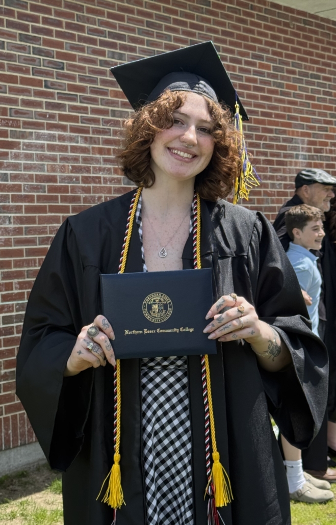 mckenzie stands wearing cap and gown at commencement, holds her diploma