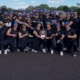 KNights team stands in black uniforms with black hats holding tournament trophy