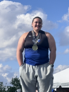 Maci stands with medal around her neck smiling at camera