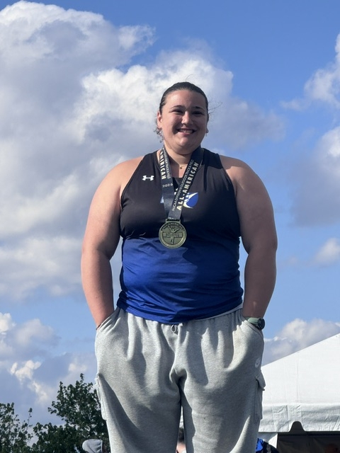 Maci stands with medal around her neck smiling at camera