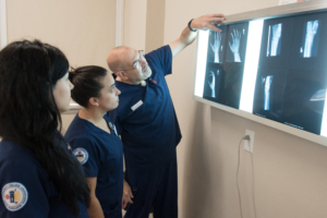instructor stands pointing at an xray of a hand while students in scrubs look on