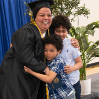 a woman wearing cap and gown hugs two children