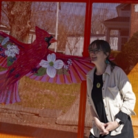 houle sits on a bus stop bench with a red bird affixed to it