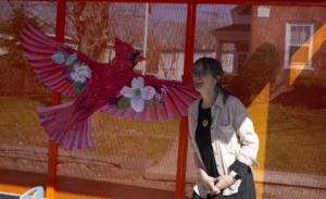 houle sits on a bus stop bench with a red bird affixed to it