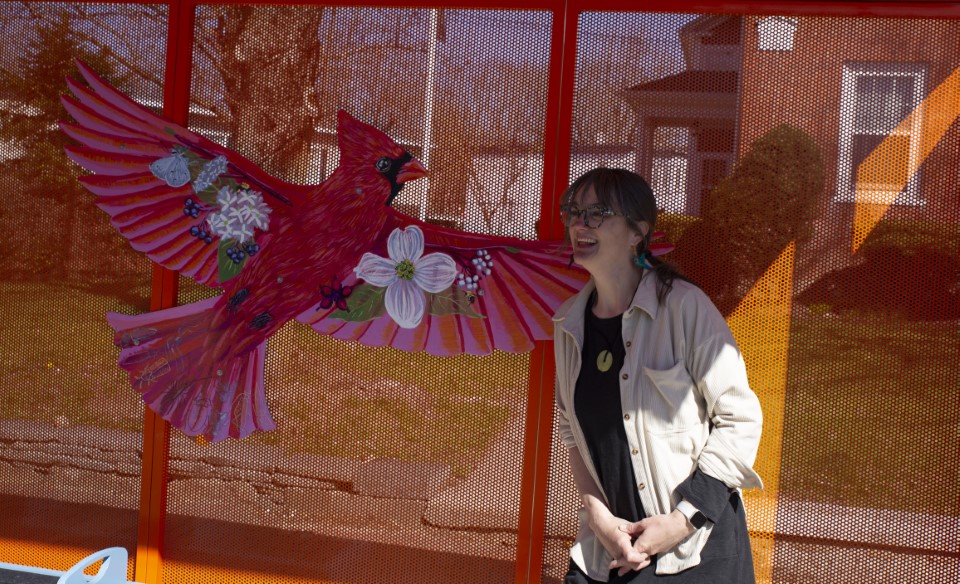 houle sits on a bus stop bench with a red bird affixed to it