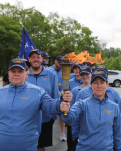 student officers dressed in blue zip shirts carry torch