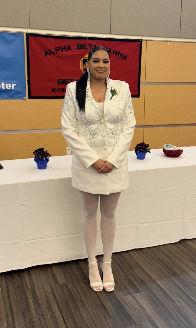 Yulissa, wearing a white dress stands in front of table at honors society induction