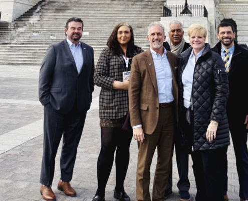 A group of adults posing and smiling for the camera in front of te steps of the capitol builing