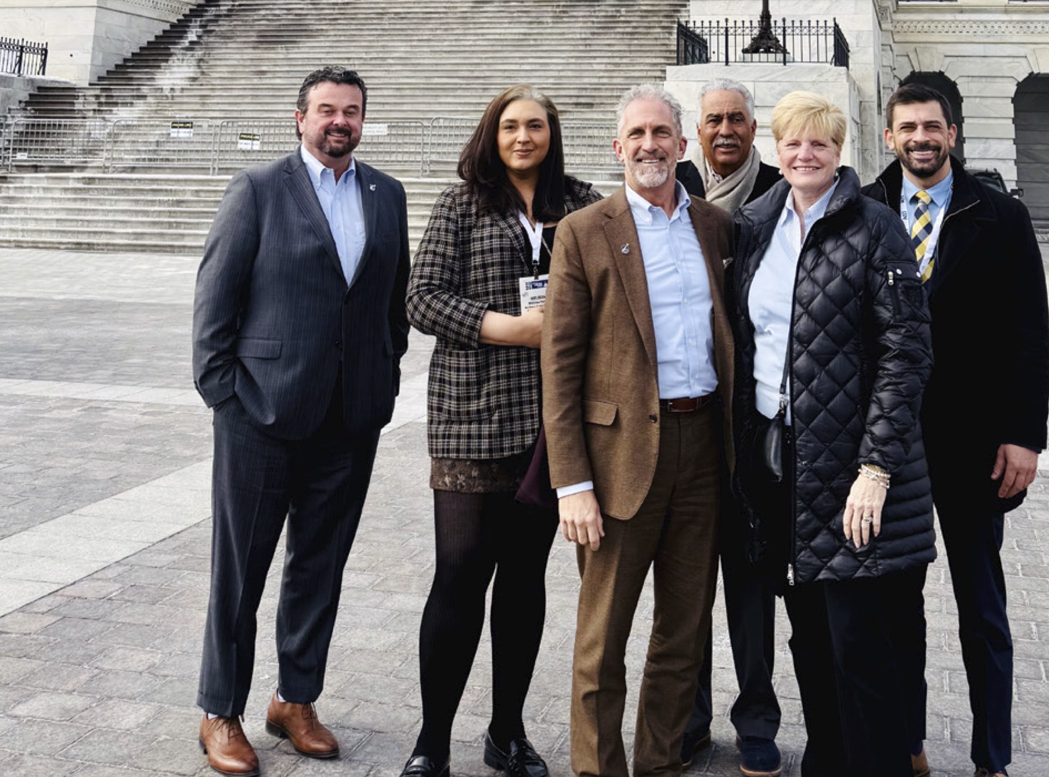 A group of adults posing and smiling for the camera in front of te steps of the capitol builing