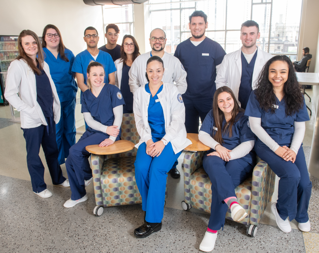 a group of nursing students pose together, many wearing dark blue scrubs