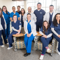 a group of nursing students pose together, many wearing dark blue scrubs