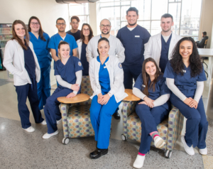 a group of nursing students pose together, many wearing dark blue scrubs