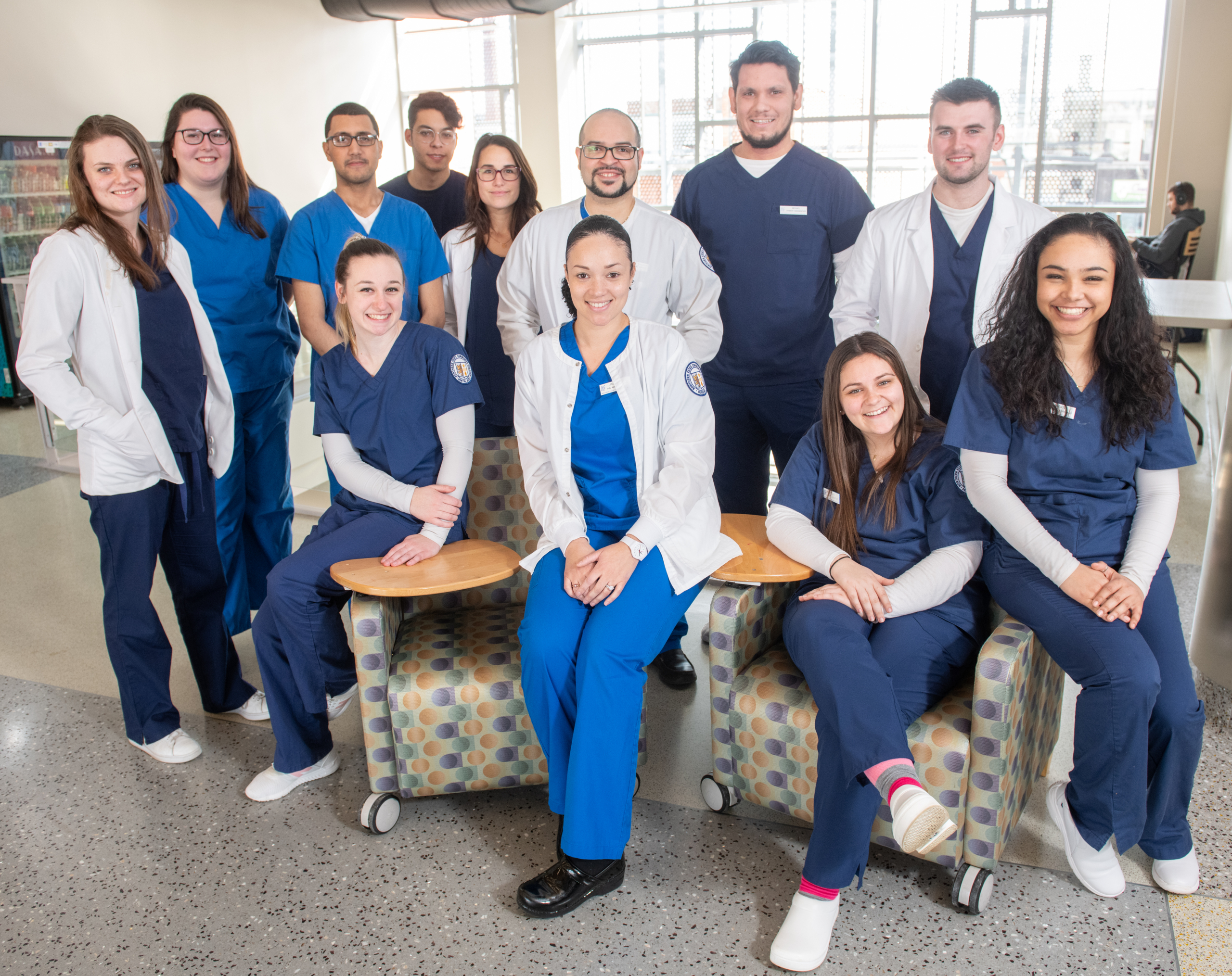 a group of nursing students pose together, many wearing dark blue scrubs