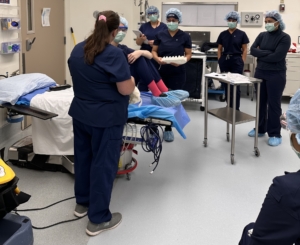students wearing blue scrubs, masks and hair covers gather together in a surgical lab
