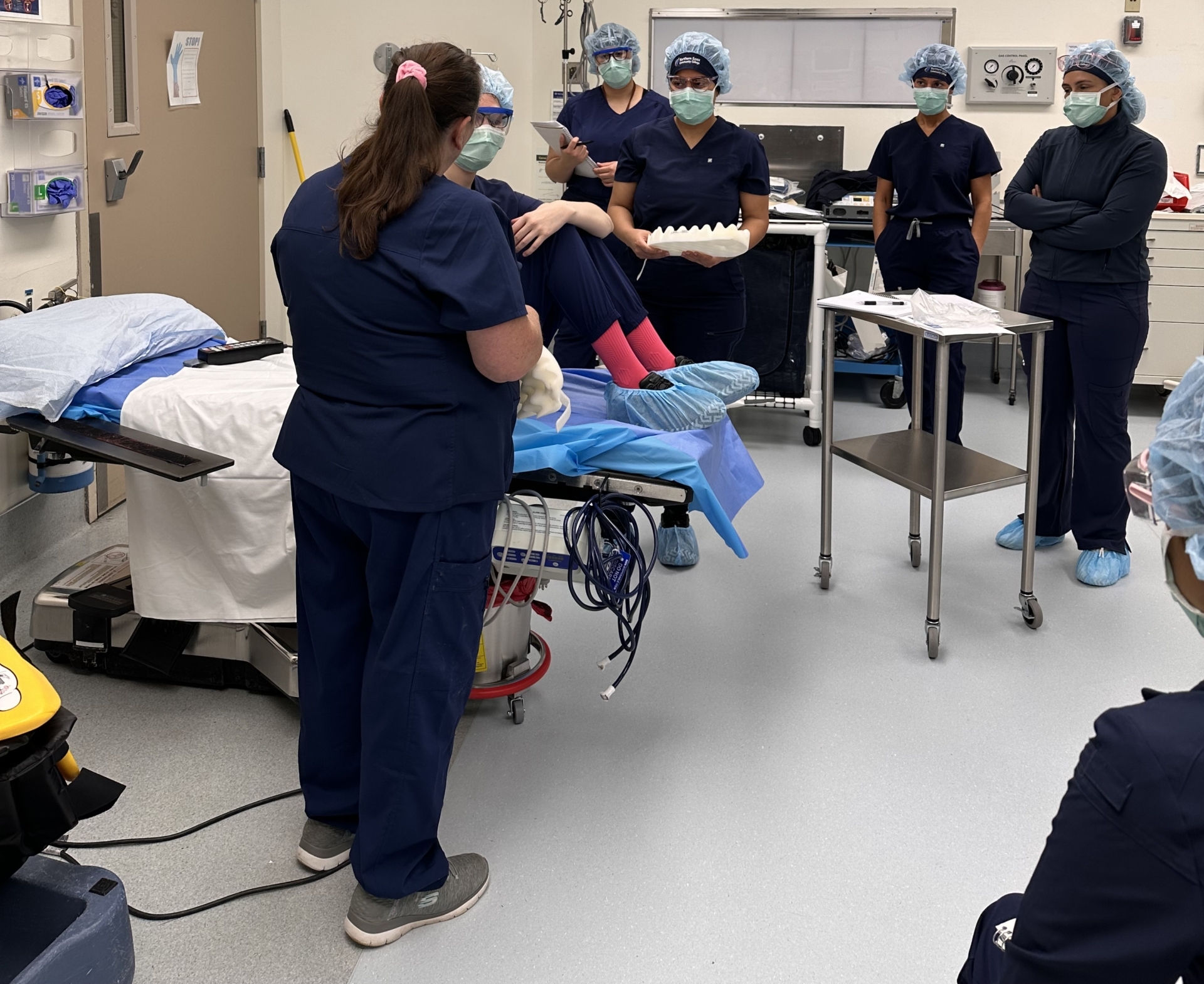 students wearing blue scrubs, masks and hair covers gather together in a surgical lab