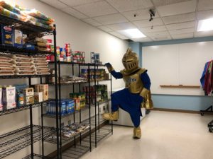NECC Knight mascot stands in the food closet looking at the dry goods.
