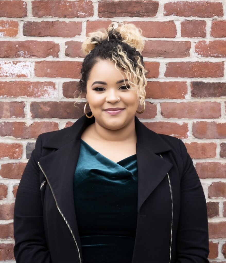 Nairoby poses against a red brick wall, smiling slightly at the camera