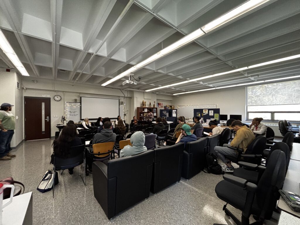 wide shot of classroom with students sitting facing a panel of four people