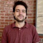 nick smiles at the camera in front of brick background