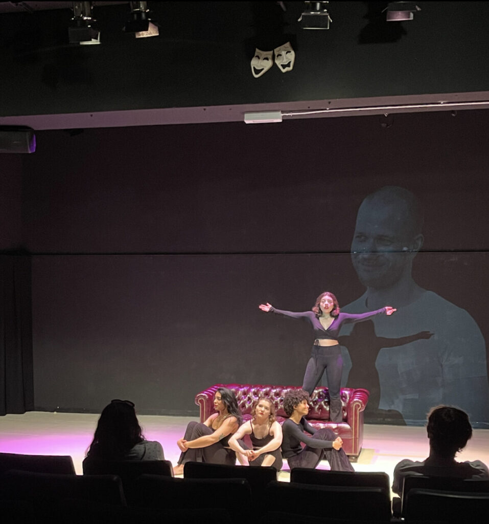Found actors sit on a stage in a spotlight, surrounding a leather couch.