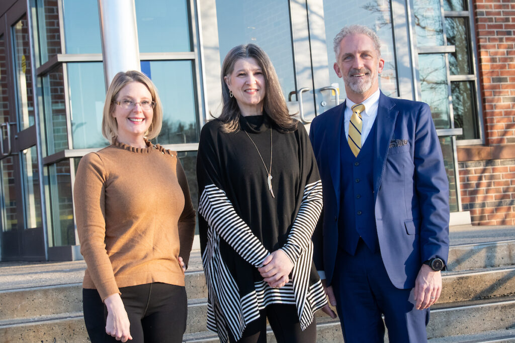 Elle and Dawn pose with President Lane Glenn outside in the steps of the tech center, they stand smiling at the camera