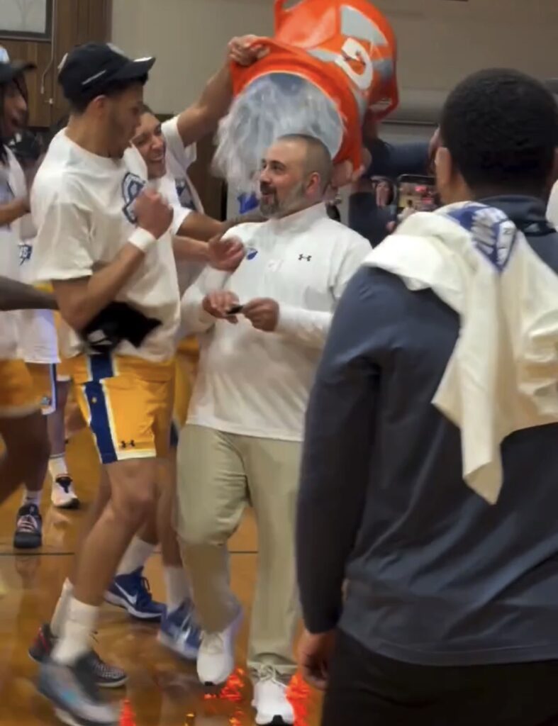 darren stratton talks to a player as two players sneak up behind him with a Gatorade bucket