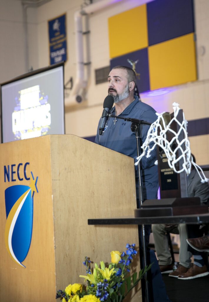 coach stratton stands at podium with trophy sitting on low table to his left