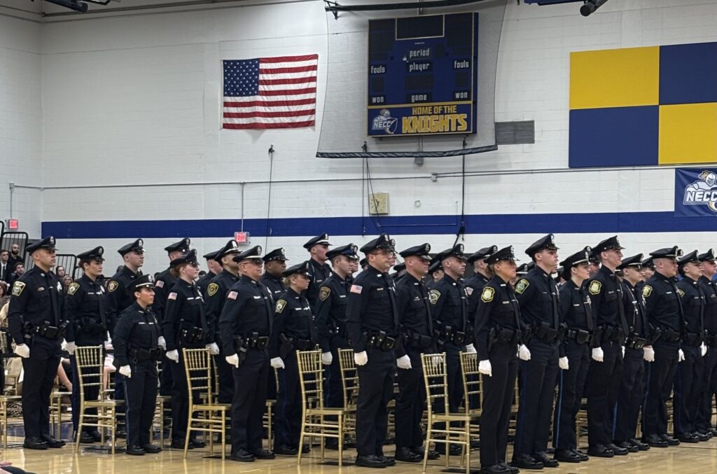 four rows of police officers stand in front of chairs, looking straight ahead