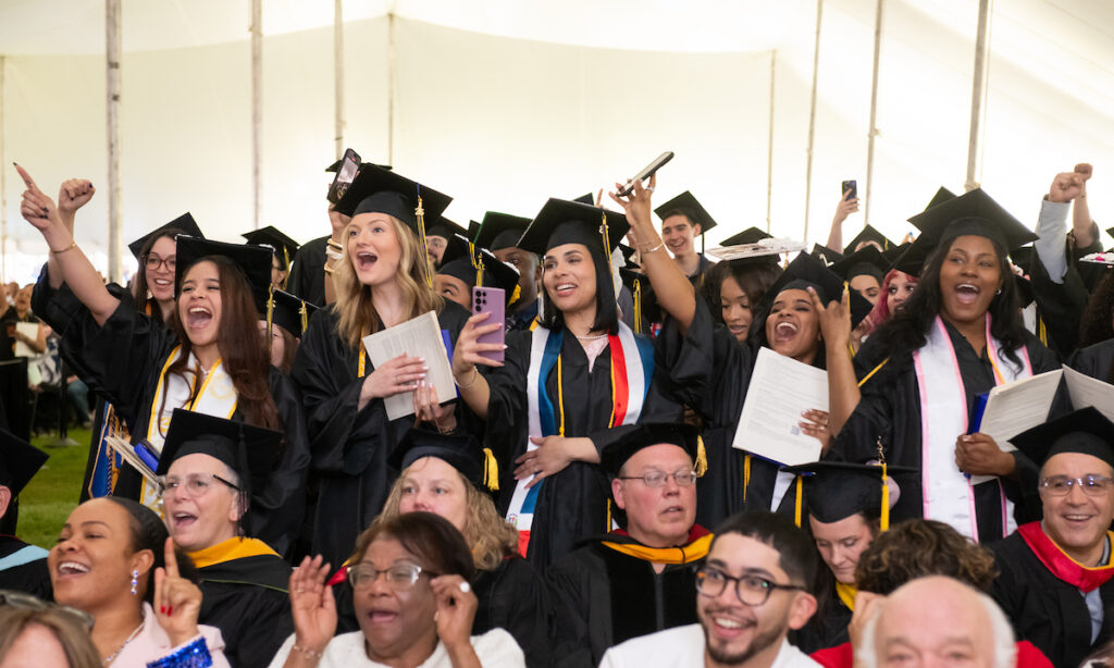 a group of graduates stand smiling with their arms in the air