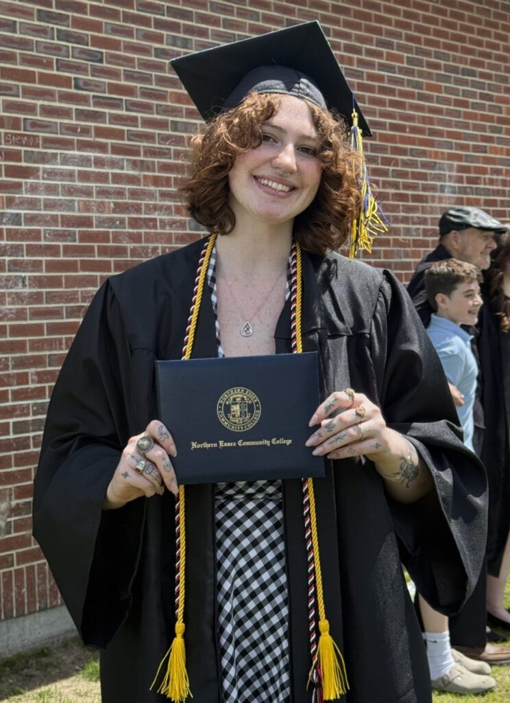 mckenzie stands wearing cap and gown at commencement, holds her diploma